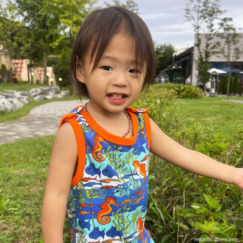 Child wearing colorful overalls with an orange trim in a park setting