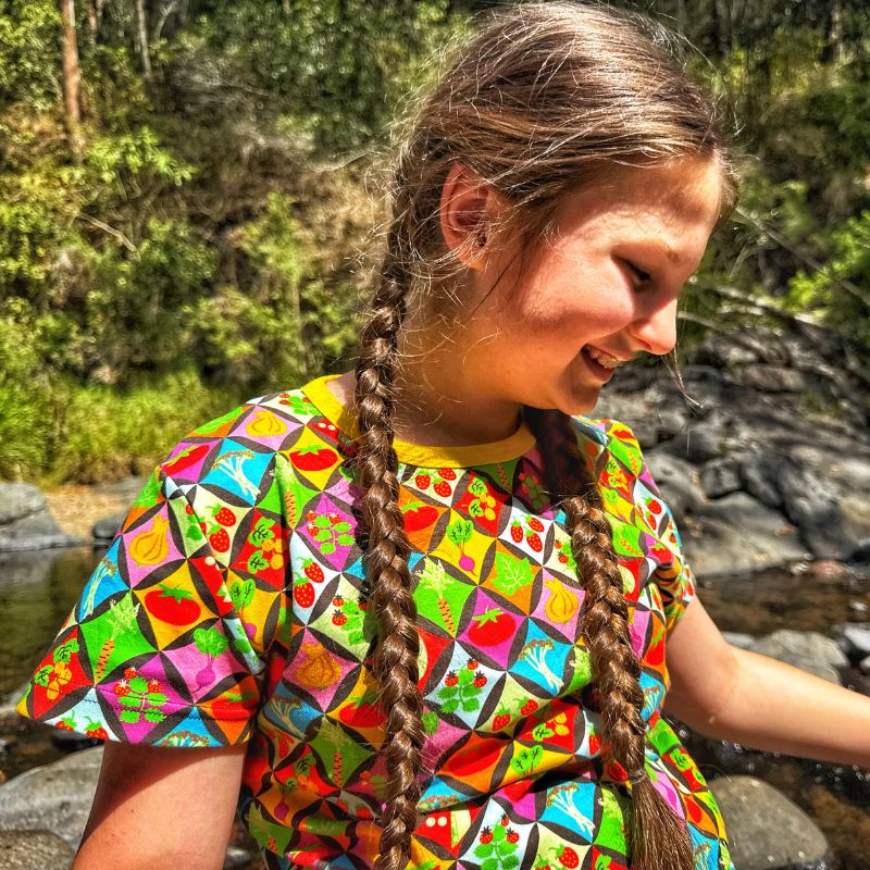 Young girl with braided hair wearing a colorful shirt in a natural setting