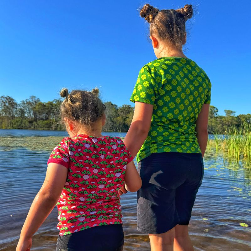 Two children holding hands by a lake with a clear blue sky.