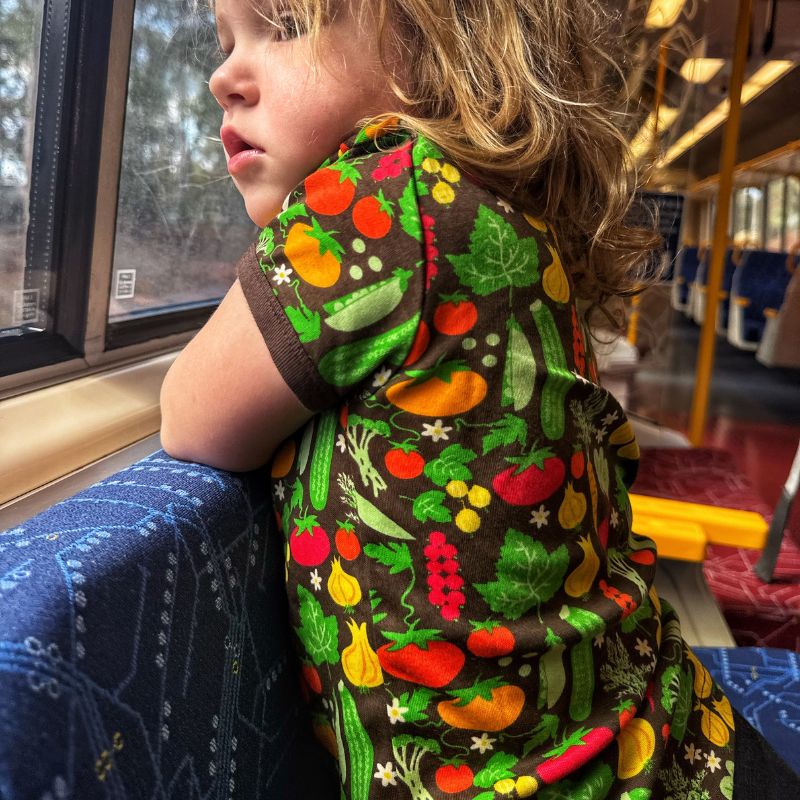 Child wearing a colorful DUNS Sweden t-shirt with vegetable patterns on a bus.