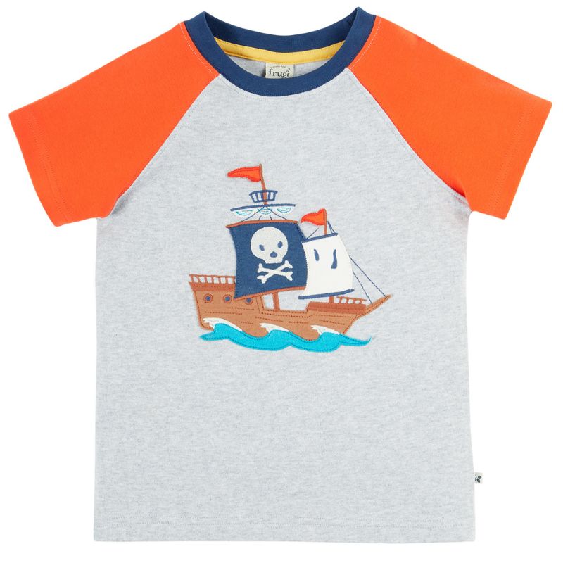 Child wearing a pirate-themed t-shirt with an orange and gray design, standing by a body of water.