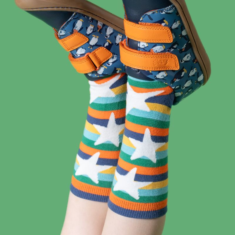 Colorful striped socks with star patterns worn with patterned shoes on a green background