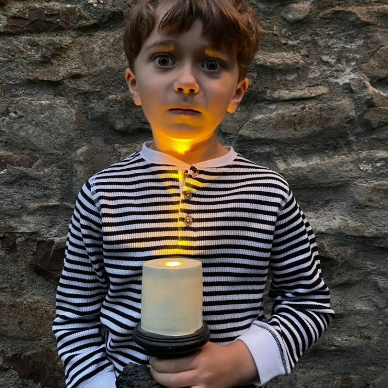 Child holding a lit candle against a stone wall