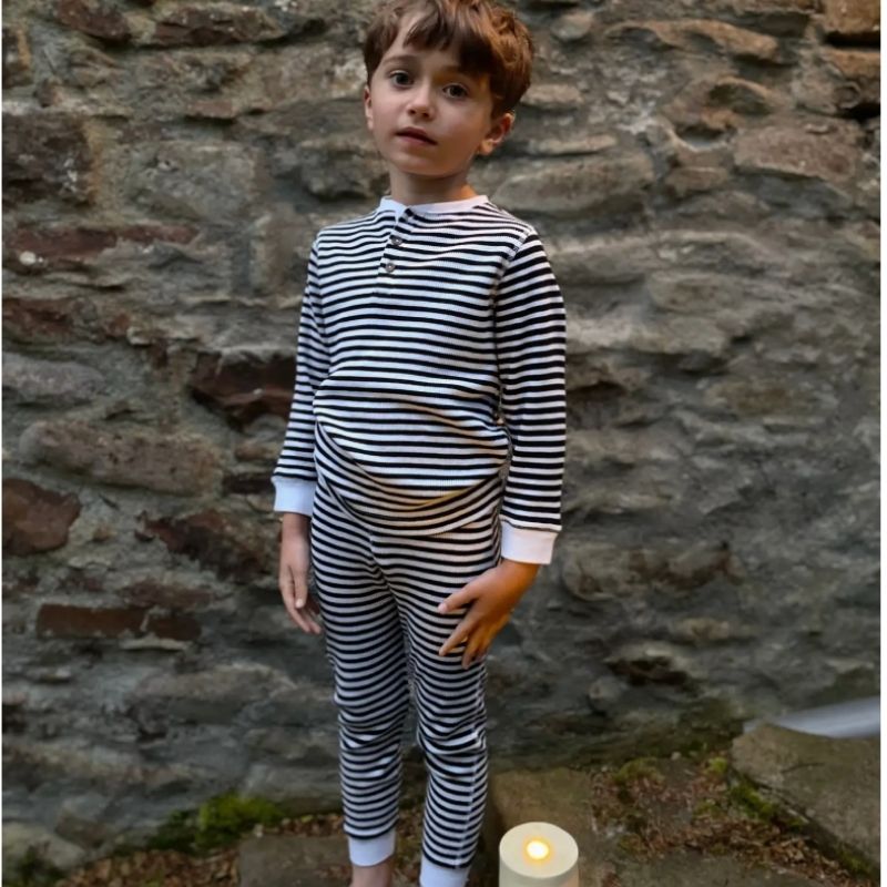 Child wearing a black and white striped outfit standing against a stone wall.