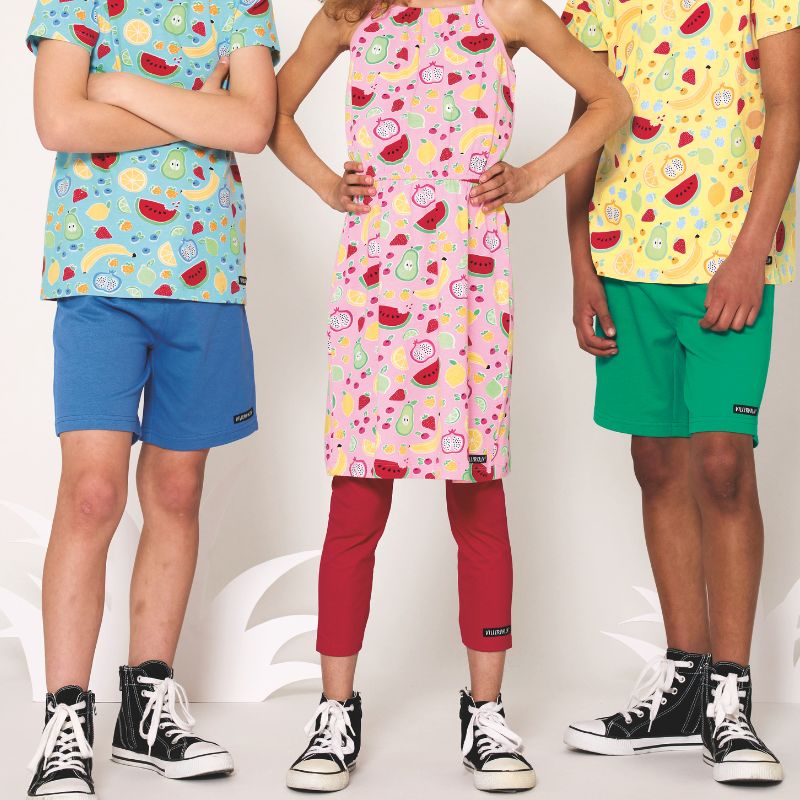 Three children wearing colorful outfits with fruit patterns on a white background