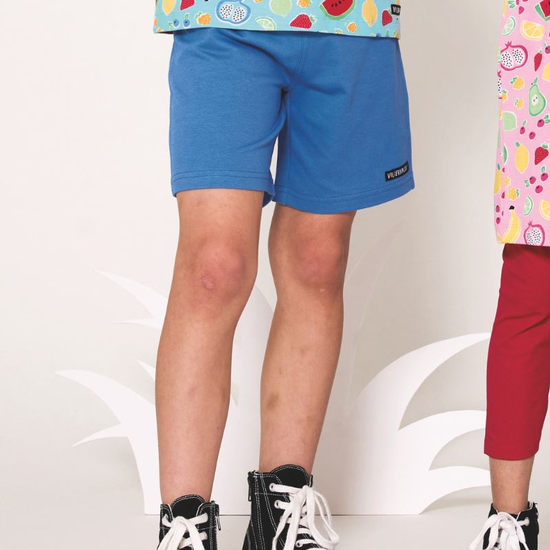 Child wearing blue shorts with a colorful top on a light background