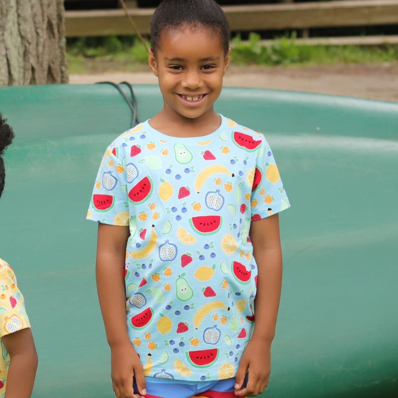 Child wearing a colorful Villervalla t-shirt with fruit patterns outdoors