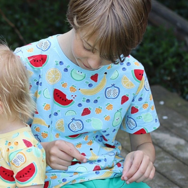 Two children wearing colorful fruit-patterned shirts outdoors.