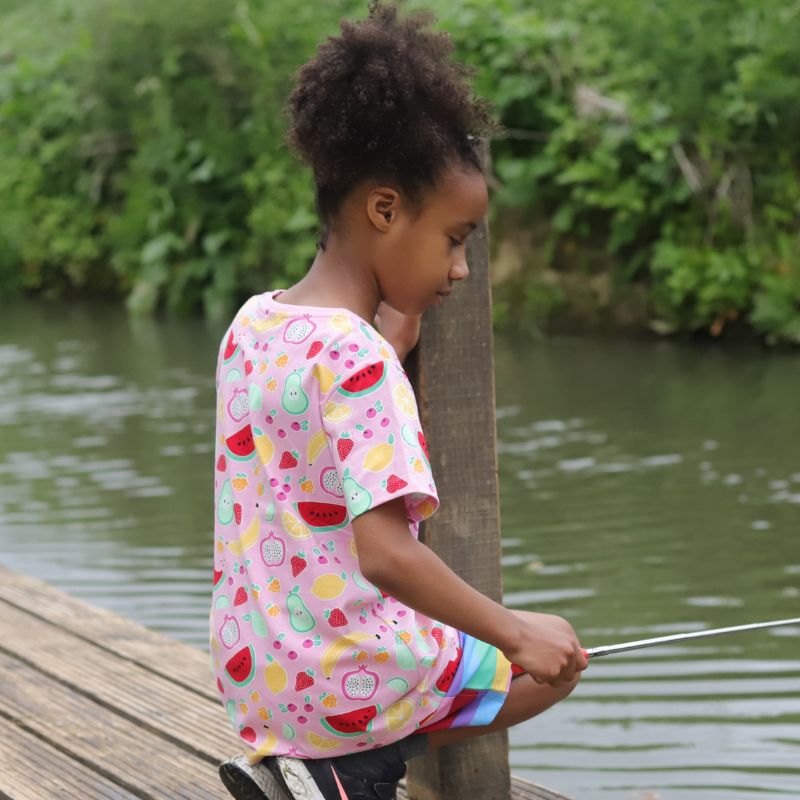 Child in a colorful fruit-print t-shirt fishing by a body of water