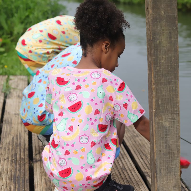 Two children in colorful outfits sitting on a wooden dock by a body of water.