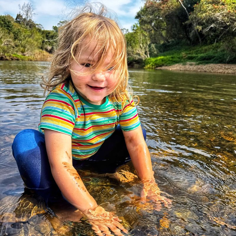 Child playing in a river with colorful Villervalla striped shirt and muddy hands