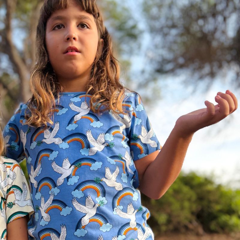 Child wearing a blue Villervalla t-shirt with rainbow, cloud and dove pattern outdoors