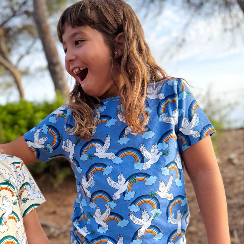 Child wearing a blue Villervalla t-shirt with rainbow, cloud and dove pattern outdoors