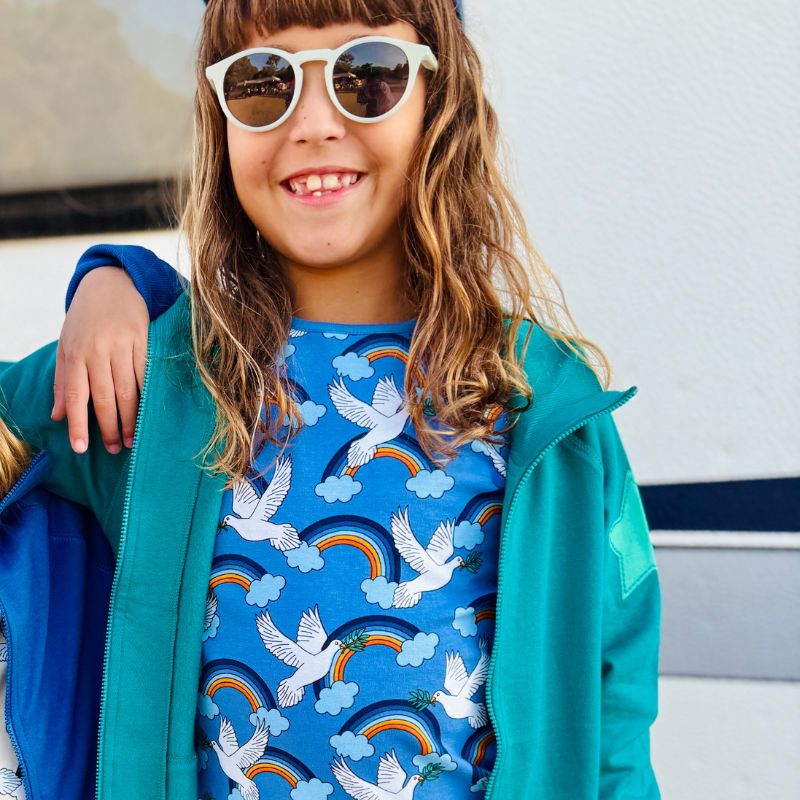 Child wearing a blue t-shirt and jacket with a colorful pattern, standing outdoors.