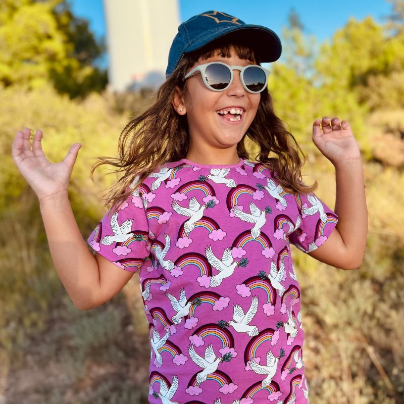 Child wearing a colorful Villervalla Peace t-shirt with rainbow and dove patterns, outdoors.