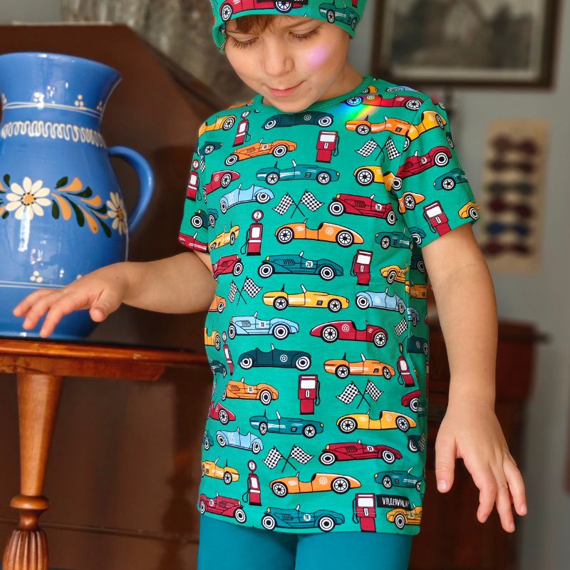 Child wearing a green Villervalla t-shirt with car patterns sitting on stairs.