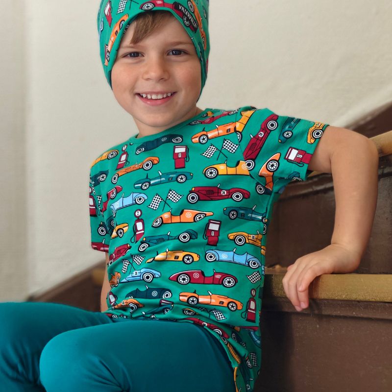 Child wearing a green Villervalla t-shirt with car patterns sitting on stairs.